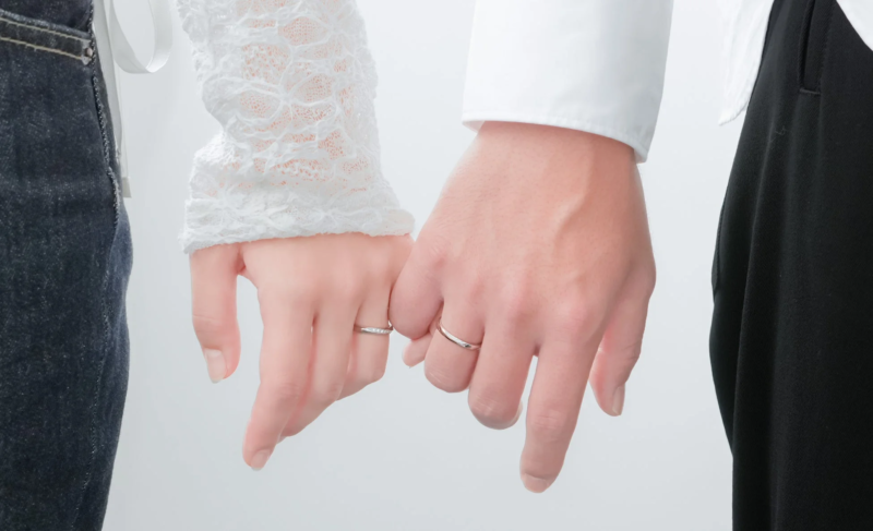 結婚指輪をはめた男女が小指を絡ませて約束を交わしている様子を捉えたクローズアップ写真