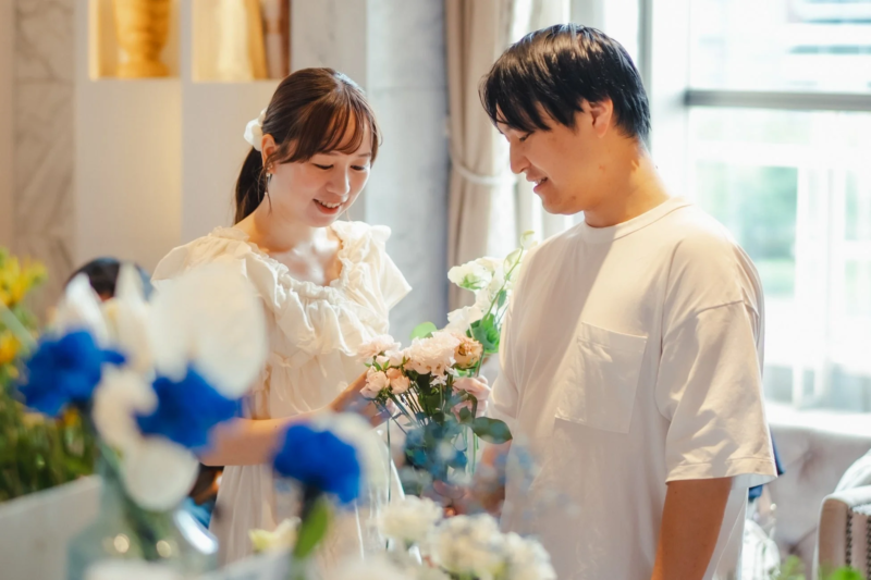 笑顔の男女が室内で一緒にフラワーアレンジメントを楽しんでいる様子です。和やかな雰囲気の中、二人は協力しながら花を飾り付けています。