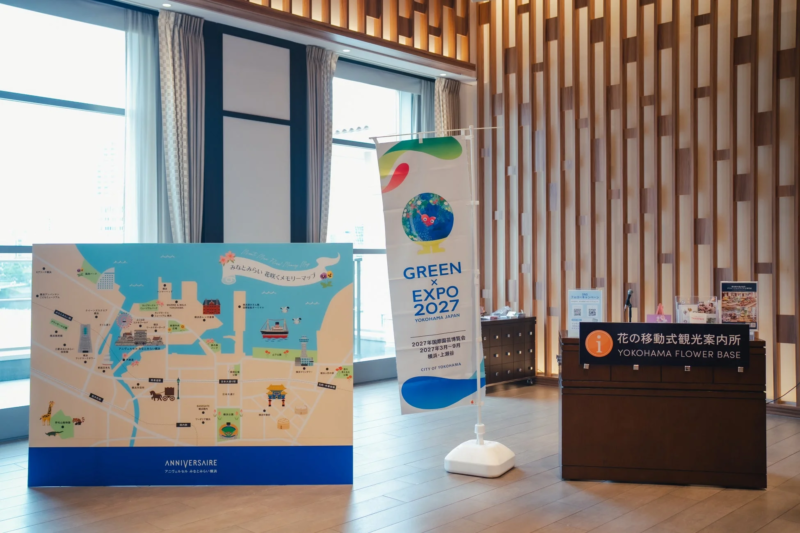 横浜みなとみらい地区の観光案内と2027年国際園芸博覧会「GREEN x EXPO 2027」の告知が行われている屋内スペース。みなとみらいの地図とイベントのバナー、そして「YOKOHAMA FLOWER BASE」と書かれた案内所が設置されている。