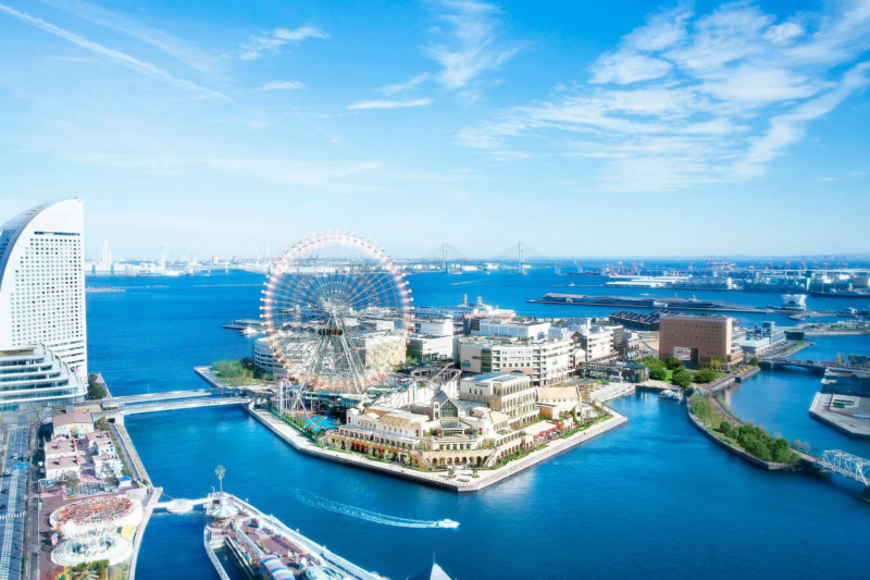 晴れた日の横浜みなとみらいのパノラマビュー。コスモクロック21の観覧車を中心に、青い海と空、そして近代的なビル群が広がる美しい都市景観です。
