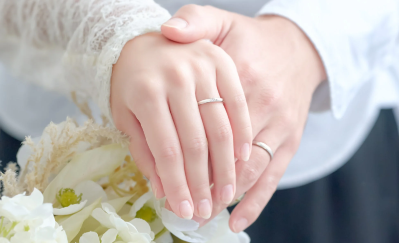 結婚指輪をはめたカップルの手が、白い花束を優しく重ねて握っているロマンチックな一枚