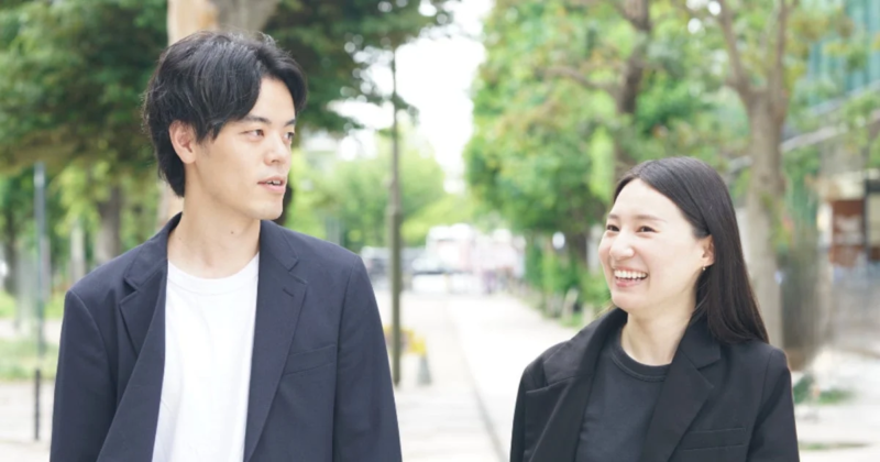 並木道を歩く男女が楽しそうに会話している様子