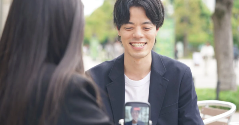 屋外で、女性が持つスマートフォンを見ながら男性が笑顔で話している様子